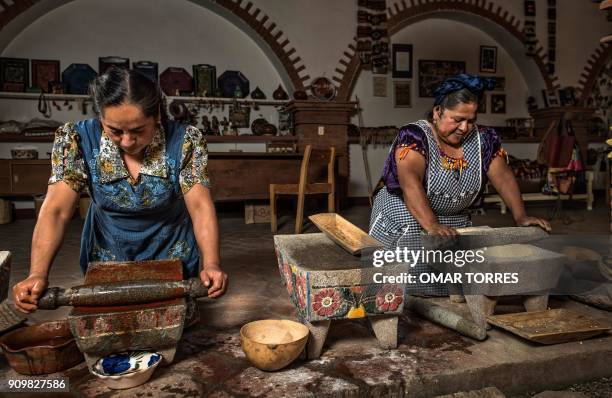 Chef Abigail Mendoza and her sister Rufina grind toasted yellow corn and chilcosle chili pepper with a Metate - a traditional grinding stone - before...
