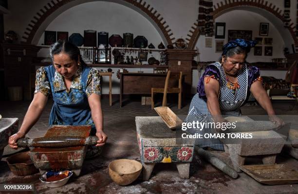 Chef Abigail Mendoza and her sister Rufina grind toasted yellow corn and chilcosle chili pepper with a Metate - a traditional grinding stone - before...