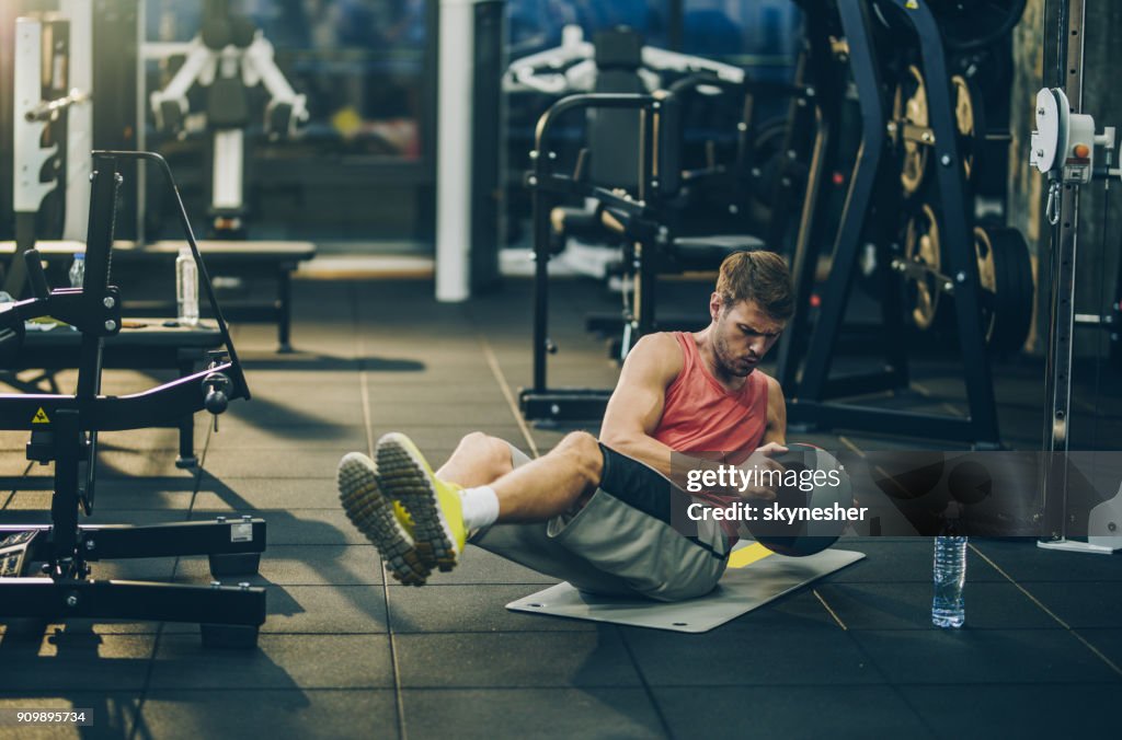 Sportlicher Mann bemüht sich beim Sit-ups mit Medizinball in einem Fitnessstudio trainieren.