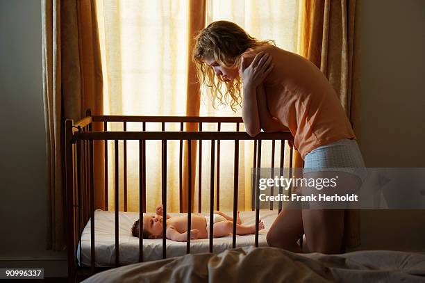 young mother looking at baby lying in cot - babybett stock-fotos und bilder