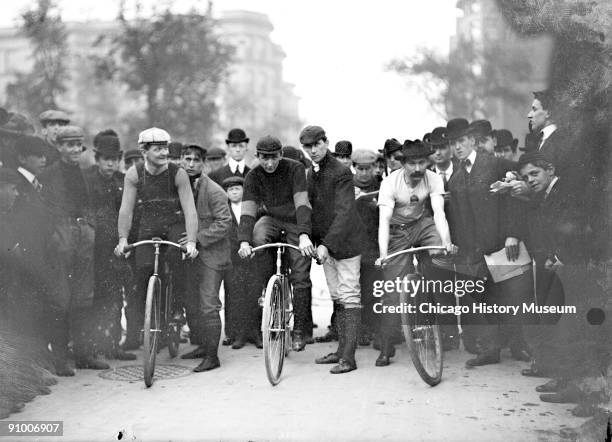 Image of cyclists, J. E. Gill, C. A. Linde, Ed Bukowski , positioning on their bicycles in front of a crowd on North Michigan Avenue in the Near...