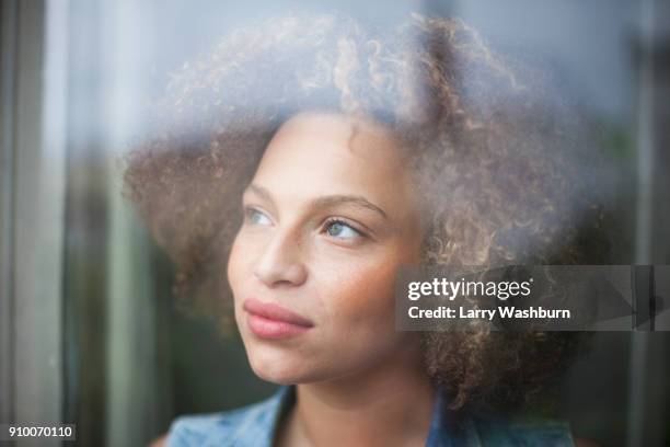 close-up of thoughtful woman with curly hair seen through glass window - looking away stockfoto's en -beelden