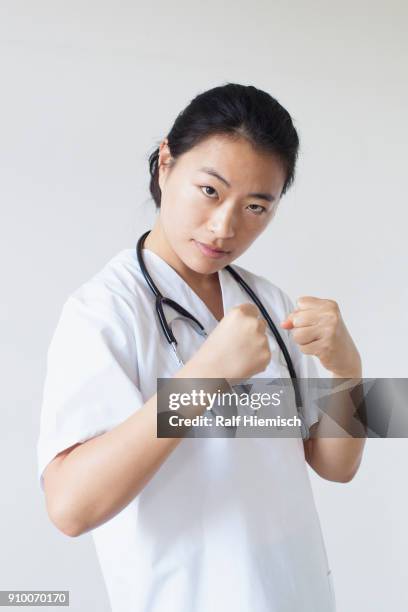 portrait of female doctor in fighting stance against white wall - kampfpose stock-fotos und bilder
