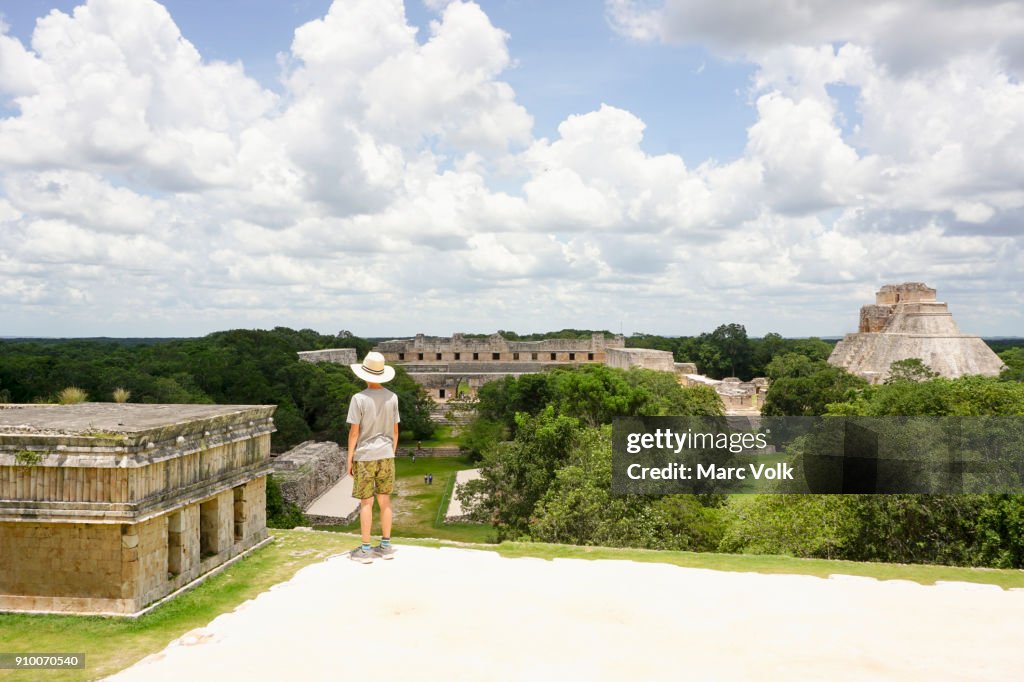Full length of boy looking at pyramids against cloudy sky, Uxmal, Yucatan, Mexico