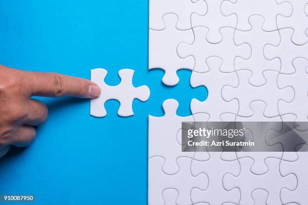 hand holding piece of white puzzle on blue background. business and team work concept. - puzzle business stockfoto's en -beelden