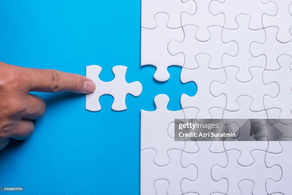 Hand holding piece of white puzzle on blue background. Business and team work concept.