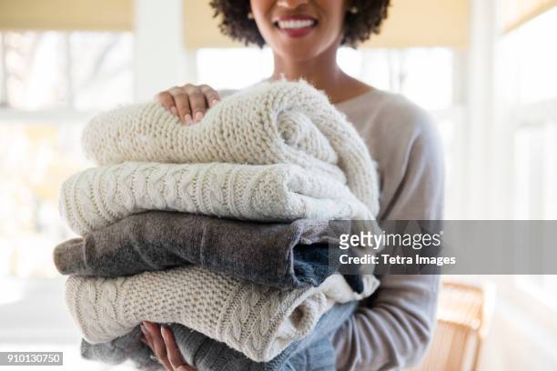 woman holding stack of folded sweaters - maglione foto e immagini stock