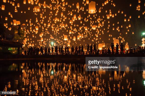 thousands of lanterns in the sky with the reflection on the water with people watching.yeepeng festival, chiangmai, thailand - religion stock-fotos und bilder