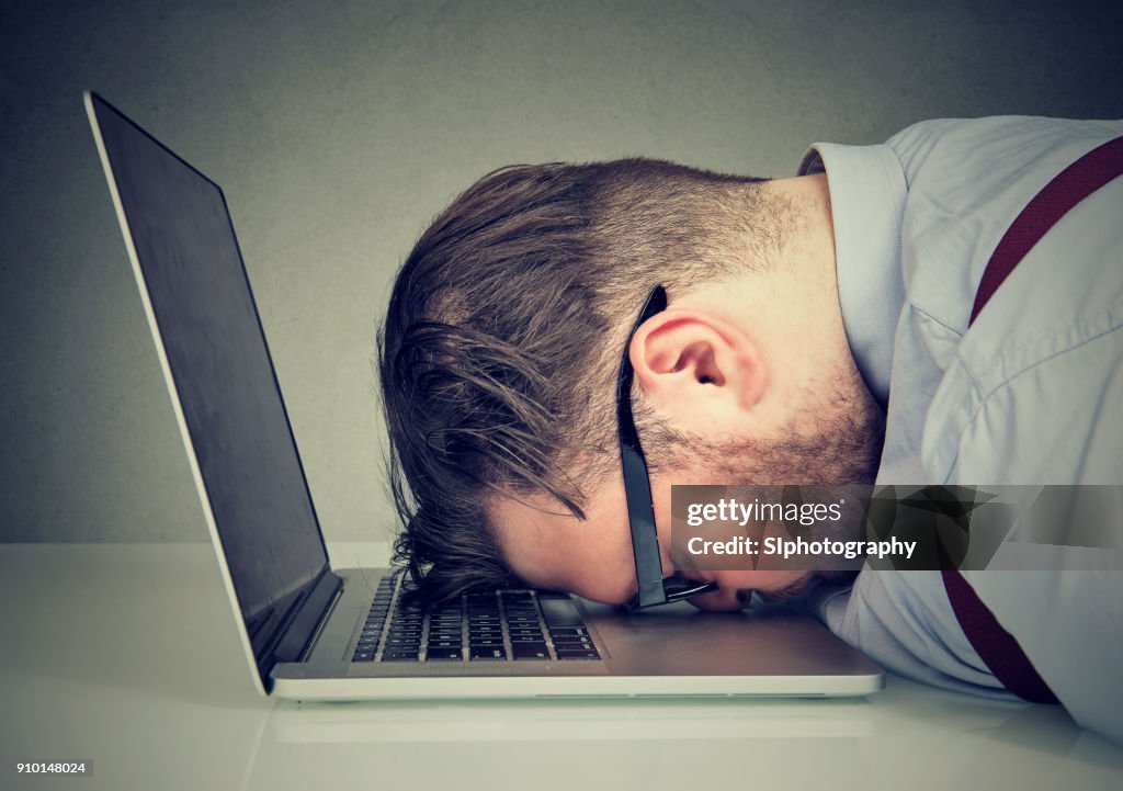 Overworked man lying on laptop