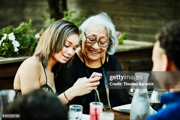 granddaughter showing grandmother photos on smartphone during outdoor family dinner - kid presenting stock pictures, royalty-free photos & images