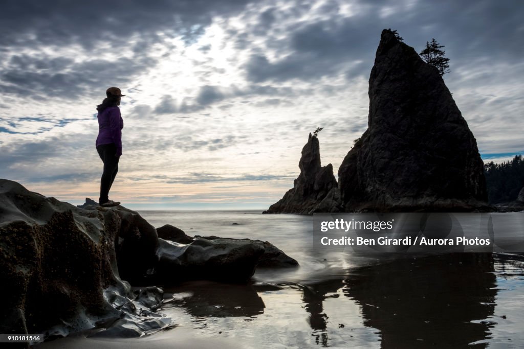 Silhouette of woman standing on rock on beach and looking at rock formation, Rialto Beach, La Push, Washington State, USA
