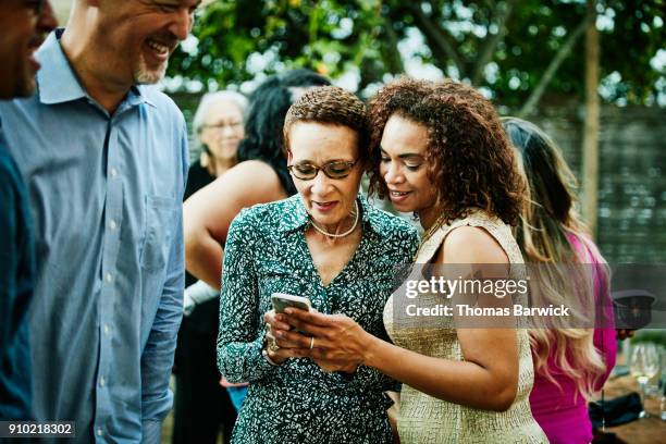 woman showing sister inlaw photos on smartphone after outdoor family dinner party - cunhada imagens e fotografias de stock