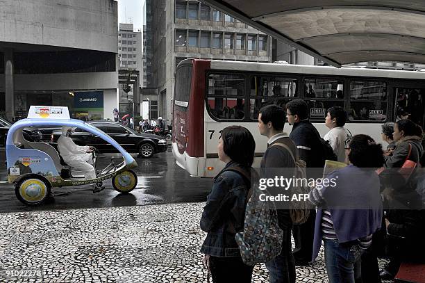 People waiting for a bus observe as an activist passes by on a prototype taxi, called 'Eco-Taxi', a covered three-wheel bicycle free of all carbon...