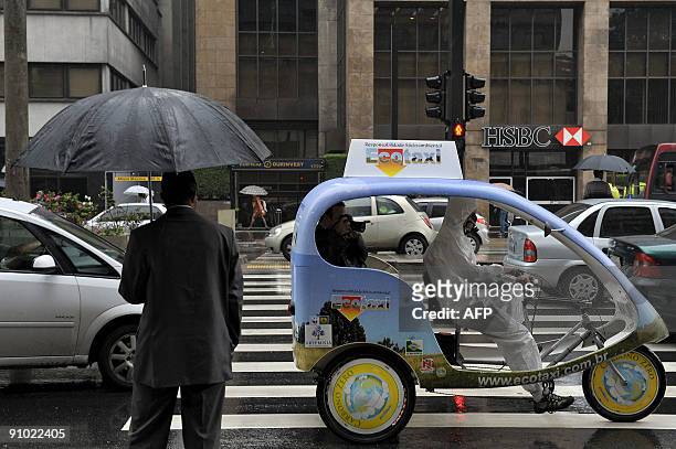 An activist carries passengers on a prototype taxi, called 'EcoTaxi', a covered three-wheel bicycle free of all carbon emissions, through the...