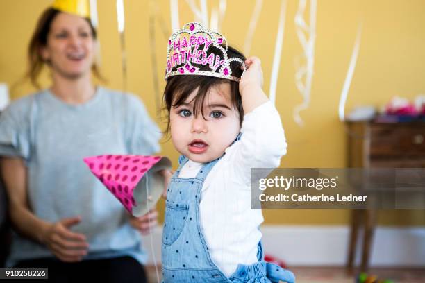 1 year old girl tugging at happy birthday crown on her head - happy birthday crown foto e immagini stock