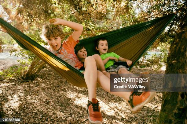 silly children play and make faces while swinging in a hammock - kicking tire stock pictures, royalty-free photos & images