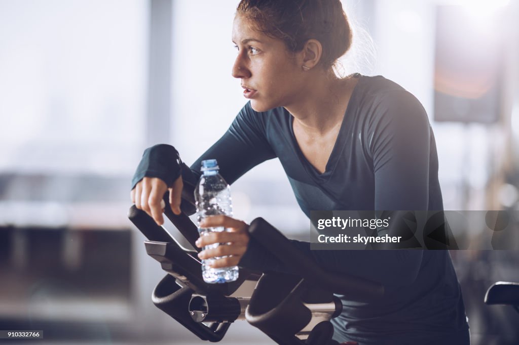 Exhausted sweaty athlete resting on water break after exercising class in a gym.