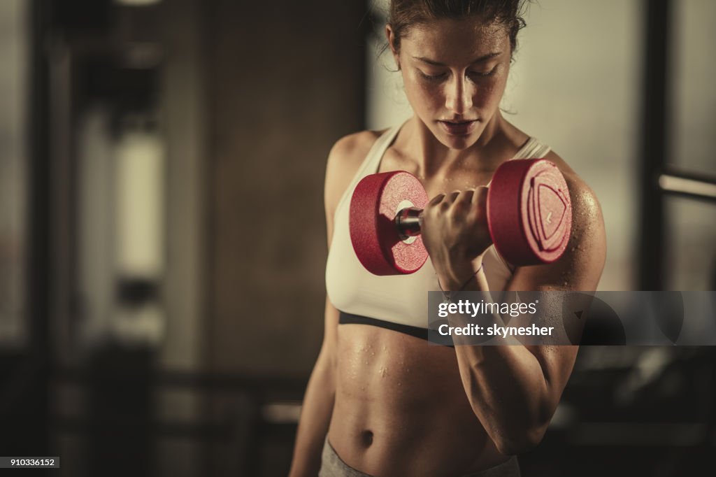Schweißtreibende sportliche Frau mit Hanteln im Fitnessstudio trainieren.