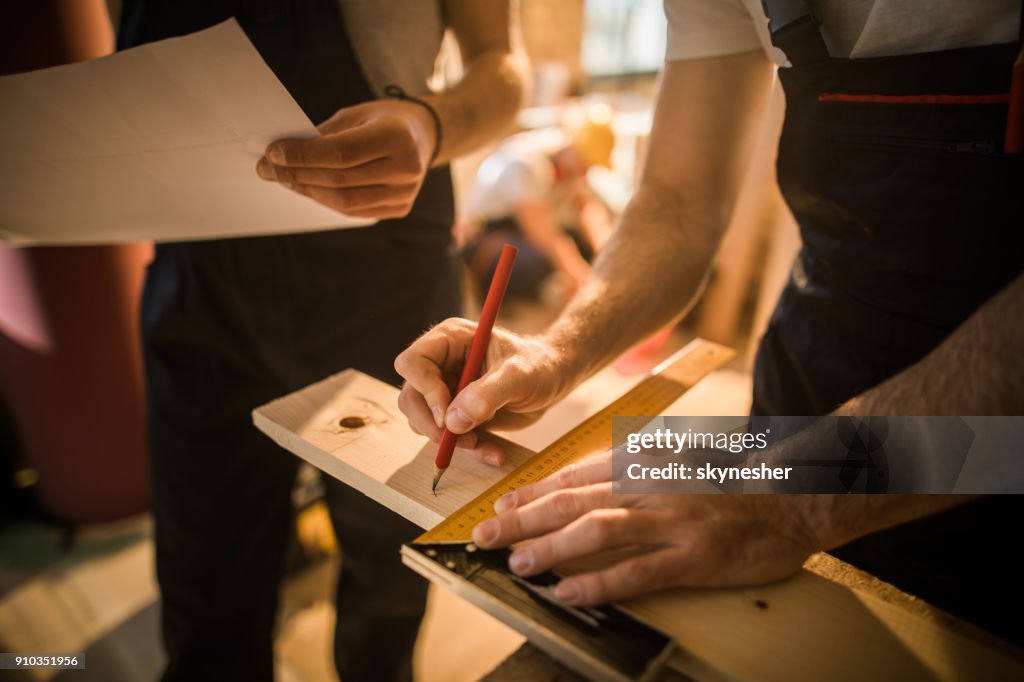 Close up of unrecognizable carpenter making measurements and drawing on a plank.