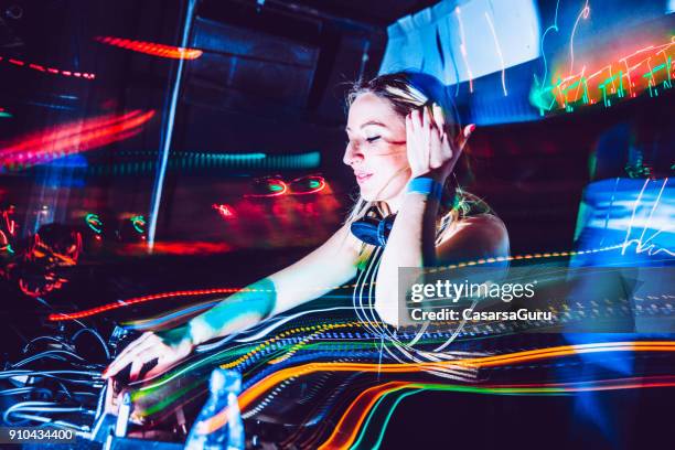 joven mujer dj escucha en los auriculares mientras escénicas - dj de club fotografías e imágenes de stock