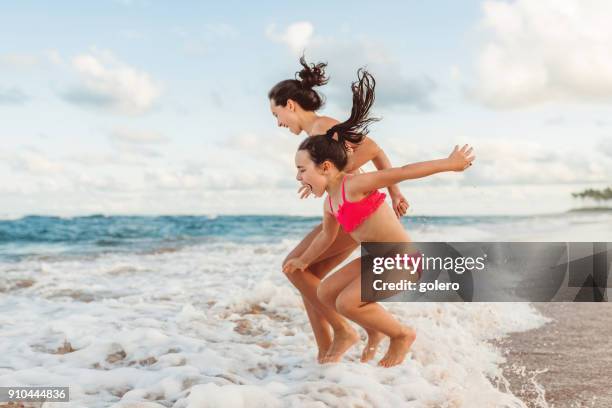 two happy sibling sisters jumping over waves - tweens in bathing suits stock pictures, royalty-free photos & images