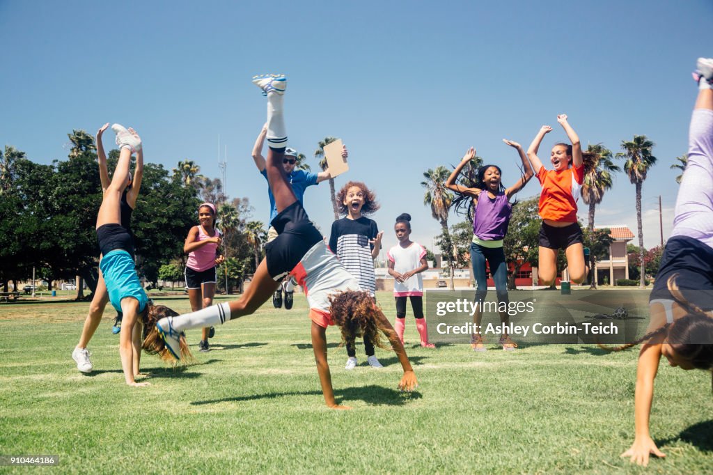 Schoolgirl soccer team doing cartwheel celebration on school sports field