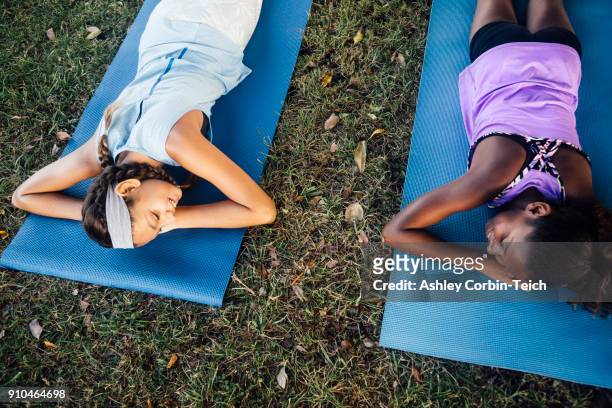 overhead view of two schoolgirls lying on yoga mats on school sports field - child yoga elevated view stock pictures, royalty-free photos & images