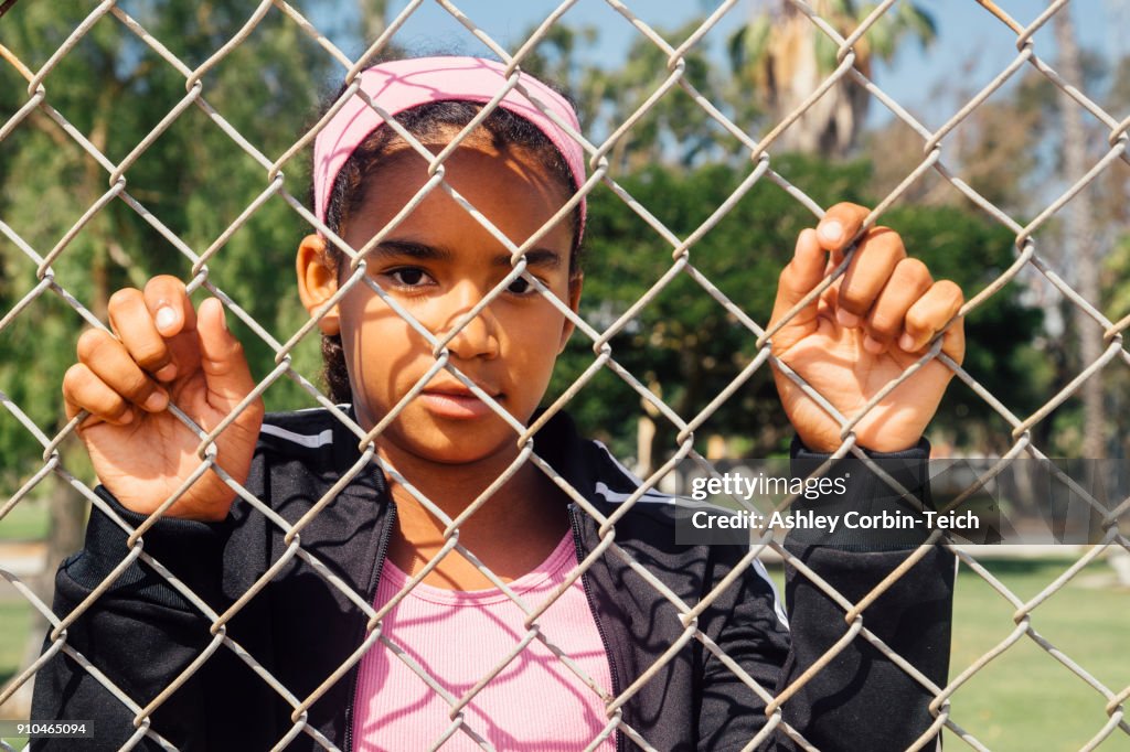 Portrait of schoolgirl holding wire fence on school sports field