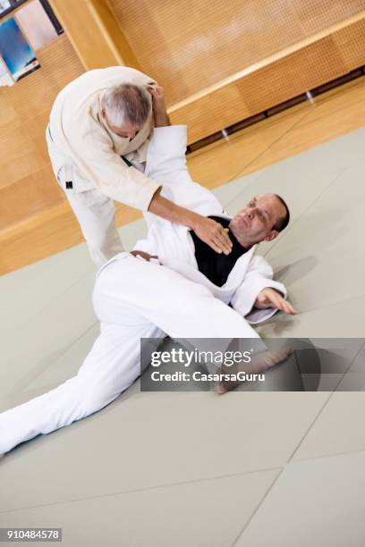 senior judokämpfer hält gegner auf den boden - takedown stock-fotos und bilder