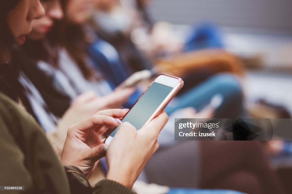 Young woman using smart phone while waiting for flight in airport lounge
