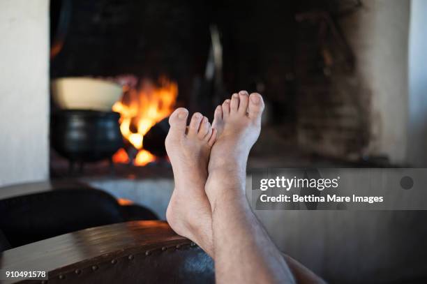 man at home with bare feet up on armchair in front of log fire, detail - mens bare feet fotografías e imágenes de stock