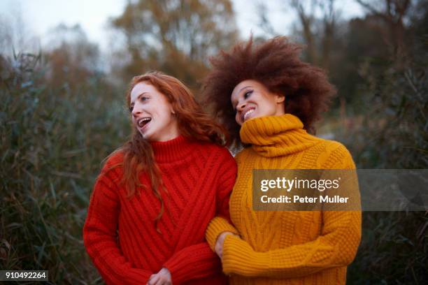 two young women, walking arm in arm along rural pathway - women's winter clothes stockfoto's en -beelden