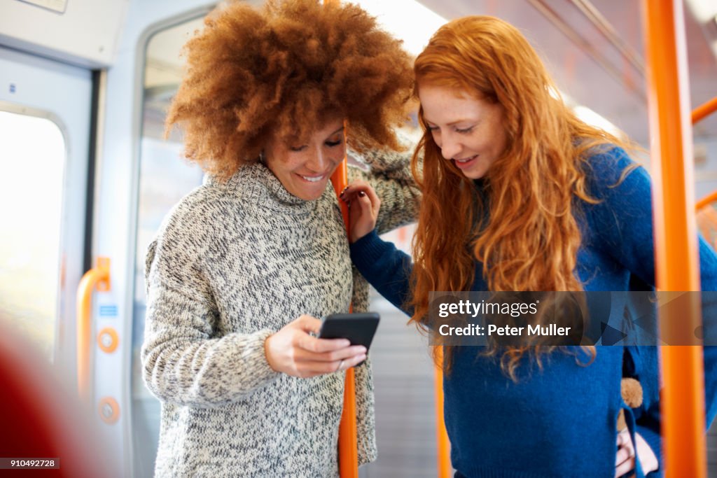 Friends sharing message on mobile phone on train, London