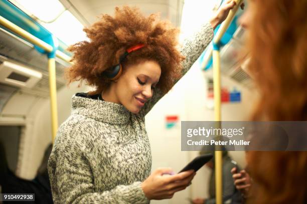 young woman on subway train, looking at smartphone - femme metro photos et images de collection