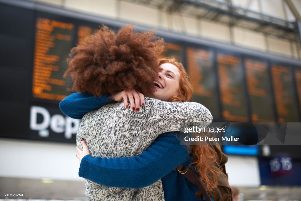 Two young women hugging at train station