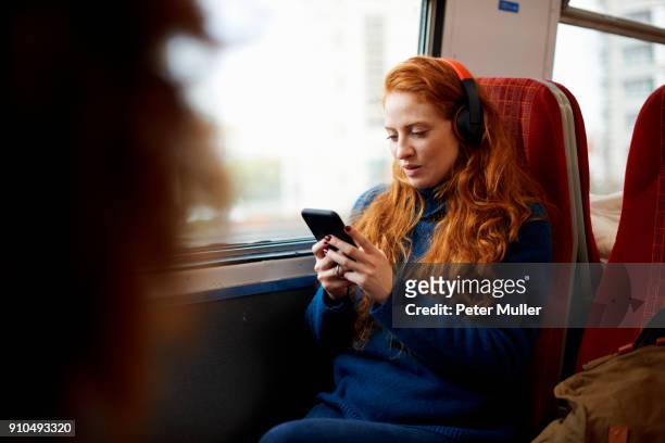 woman on train listening to music on mobile phone with headphones, london - smartphone im zug stock-fotos und bilder
