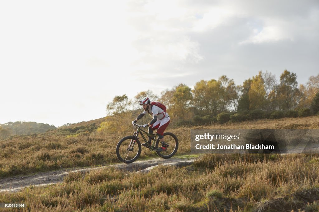 Male mountain biker biking down moorland track