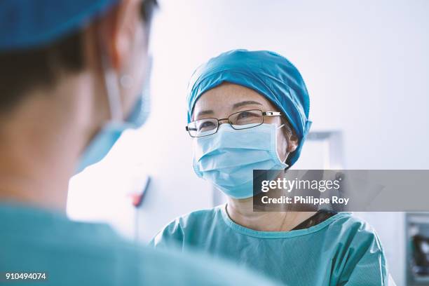 over shoulder view of surgical team wearing scrubs having discussion in maternity ward operating theatre - asia surgery stock pictures, royalty-free photos & images