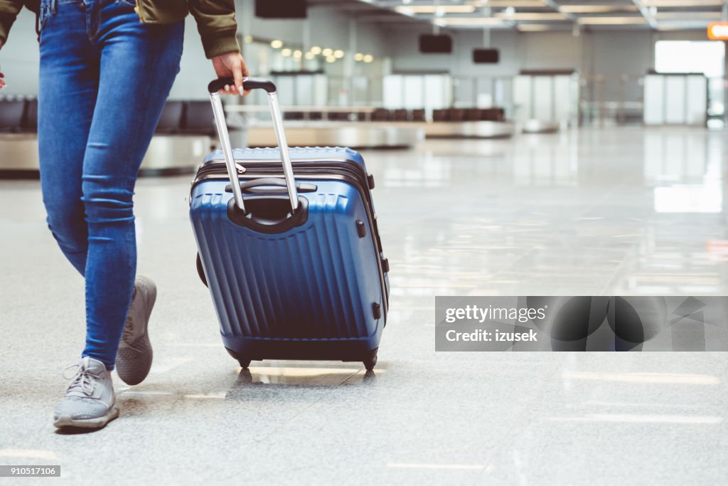 Kvinnan promenader med resväska på flygplatsterminalen