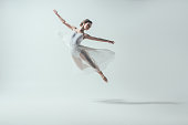 elegant ballet dancer in white dress jumping in studio