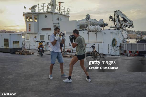 By the Port of Lampedusa, an off-duty Coast Guard crew spar boxing. .