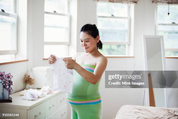 a pregnant woman in a babys nursery room, folding baby clothes. - black hair dresser stock pictures, royalty-free photos & images