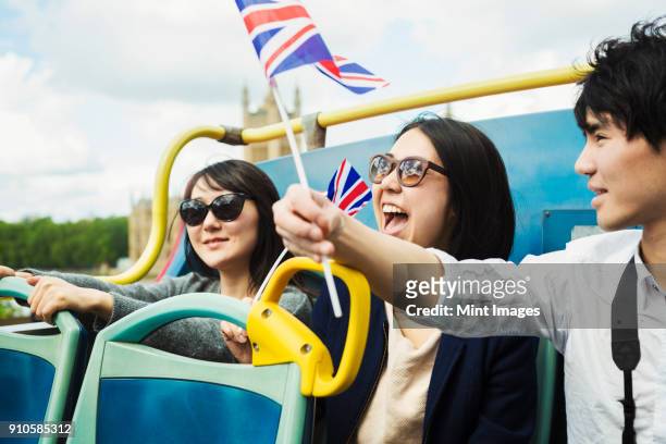 smiling man waving union jack flag and two women with black hair sitting on the top of an open double-decker bus. - only japanese stock-fotos und bilder