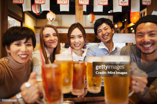 five people sitting side by side at a table in a restaurant, holding large glasses with beer. - man sipping beer smiling stockfoto's en -beelden