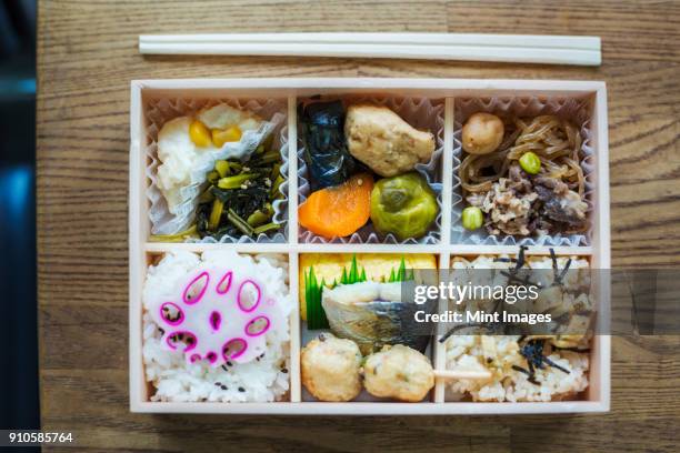 high angle close up of bento box with traditional japanese foods and chopsticks on a wooden table. - bento box stock pictures, royalty-free photos & images