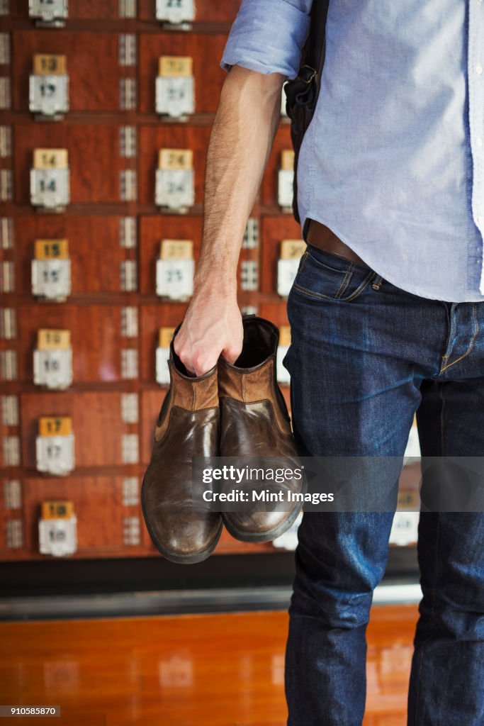 A man holding boots in his hand, shoe lockers in rows behind him.