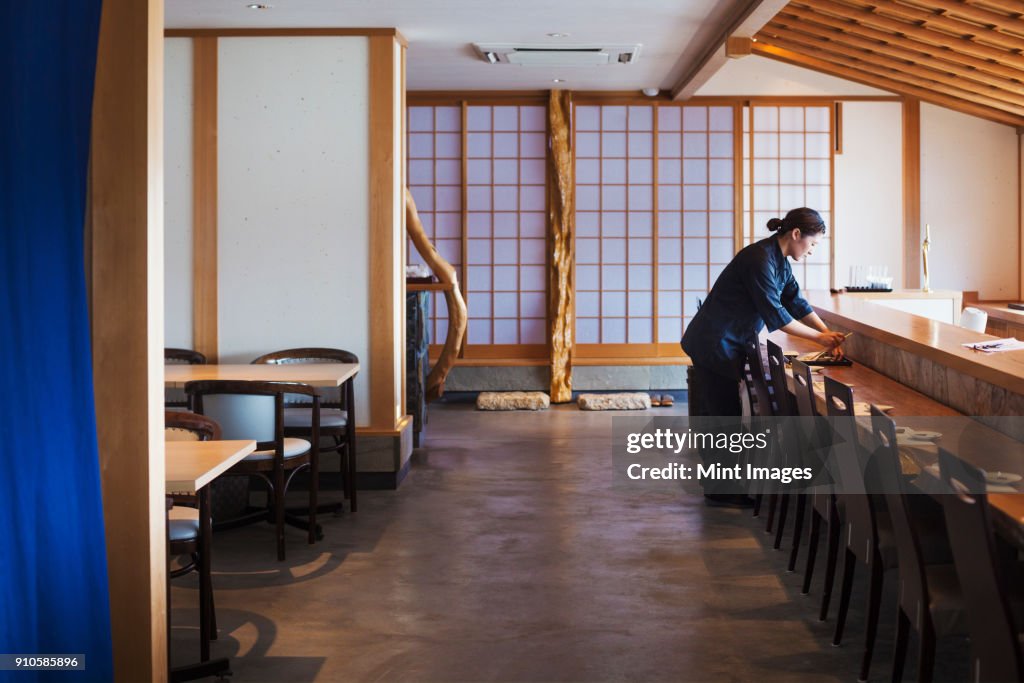 Waitress standing at a counter in a Japanese sushi restaurant, preparing place settings.