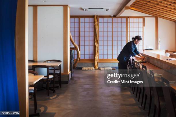 waitress standing at a counter in a japanese sushi restaurant, preparing place settings. - 飲食店 ストックフォトと画像