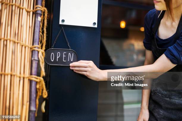 close up of woman turning open sign on glass door to a bakery. - open sign stock pictures, royalty-free photos & images