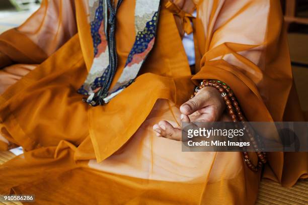 close up of buddhist monk wearing golden robe sitting cross legged on the floor, meditating, buddhist hand gesture. - mudra stock-fotos und bilder